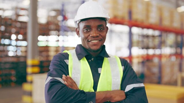 Handsome african man and happy professional worker wearing safety hard hat, Smiling and looking to camera. Big warehouse with shelves full of stock