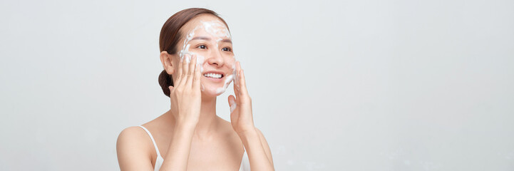 Crop cheerful young woman smiling while cleaning face with foam during skincare procedure. panorama