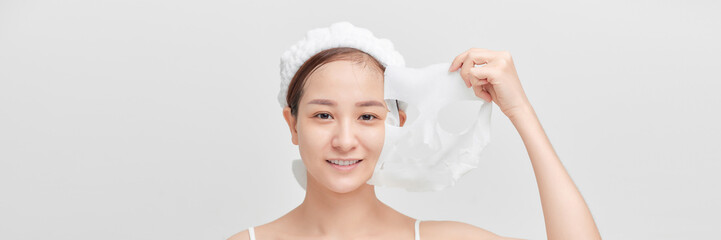 Happy young removing from face skincare hydrating sheet mask with collagen, hyaluronic acid for glowing skin