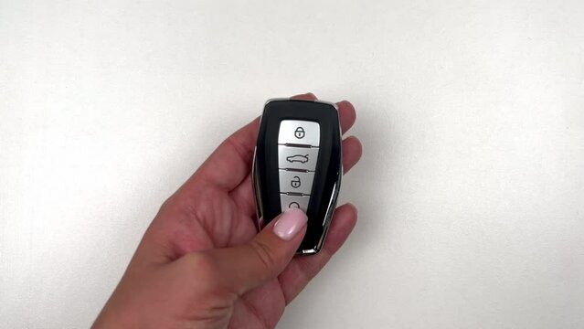 A black car key with metal inserts and automatic buttons is taken by the hand of a person of European appearance, runs his fingers over the buttons, presses the car opening icon and puts the key back
