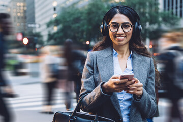 Delighted female in headphones and eyeglasses typing on mobile
