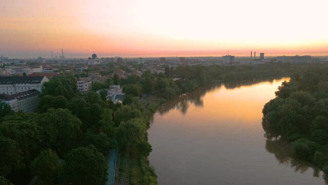 Aerial footage over Arad city center, above the park and the river Mures. Video was shot from a drone, in the morning at sunrise, while flying backwards with camera level.
