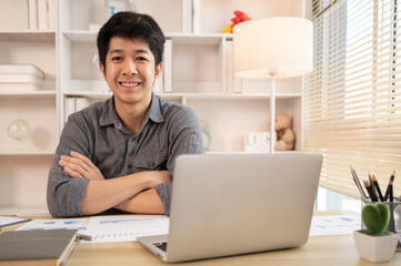 Handsome young man sits working at a desk with a laptop and office equipment, Smiling young man ready for work at the start of the week. Positive Start to a Productive Workweek.