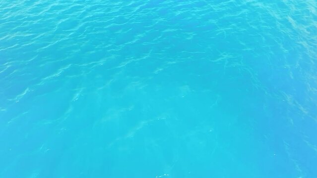 Sea wave close up, low angle view. Sea from the drone. Abstract background of flow of sea water in sunlight. Blue ocean surface. Delicate ripples on the surface of the water with refraction of light.