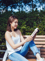 Naklejka premium Young Asian woman reading book on bench in park