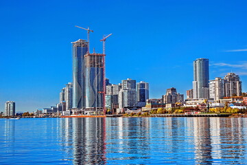 Fototapeta na wymiar New Westminster, British Columbia, Construction of high-rise buildings in the city center on the Fraser River waterfront, against a clear blue sky