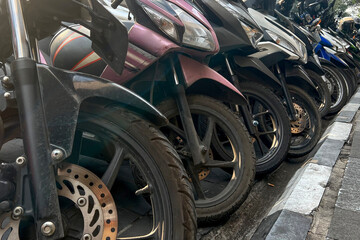 Motorbike, motorcycle scooters parked in row in city street. Close up of wheel.