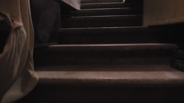An old dusty concrete staircase littered with boxes and junk along the edges. Camera moves up above the stairs. A light bulb blinks on and off, setting up the horror