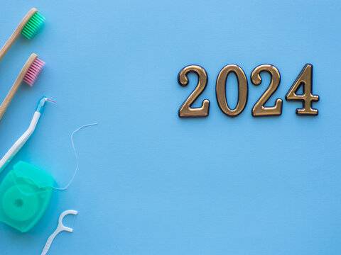 2024 and dental concept. Close up view of photo with 2024, dental floss and two wooden toothbrush on blue background with copy space. Christmas medical card. Merry Christmas and Happy New Year.