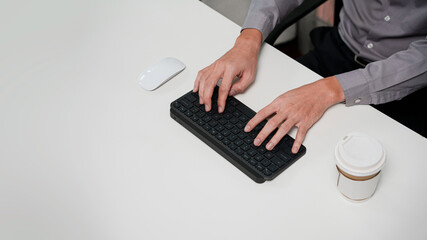 Fototapeta na wymiar Top view closeup of businessman hands typing writing and using laptop desktop computer wireless keyboard and mouse on white table in business workplace working on document research wearing shirt