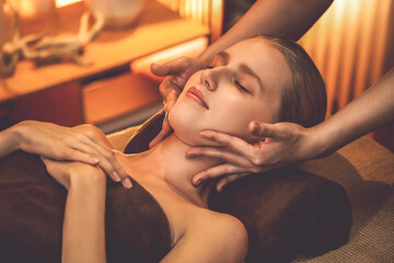 Caucasian woman enjoying relaxing anti-stress head massage and pampering facial beauty skin recreation leisure in warm candle lighting ambient salon spa in luxury resort or hotel. Quiescent - obrazy, fototapety, plakaty