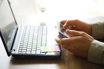 Hands using laptop and phone for online shopping, close up clean image in front of the window in soft light