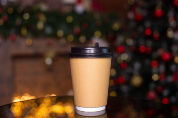 A disposable coffee cup with a lid on the background of a Christmas tree. Place for advertising