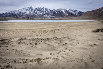Distance view of semi-frozen Kyagar Tso Lake, surrounded by snow-capped mountains.
