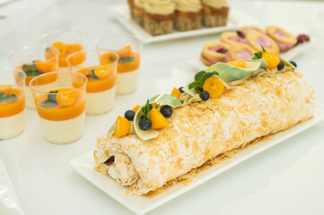 Meringue roll with decor and kumquat stands in a candy bar with tangerine panna kota
