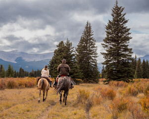 A man and woman horseback riders make their way along a trail in the Ya Ha Tinda Ranch in Alberta, Canada during autumn - obrazy, fototapety, plakaty