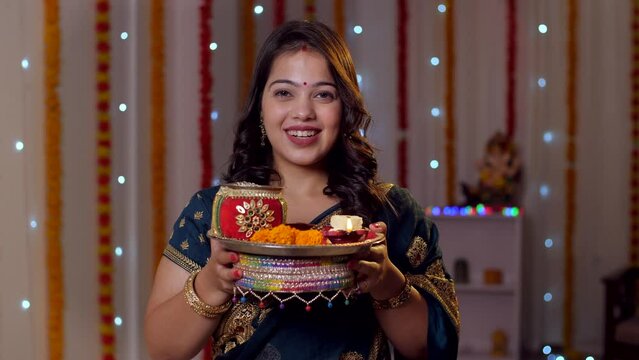 Beautiful Indian woman smiling at the camera on the occasion of Karwa Chauth - Indian rituals  posing for camera. A young lady holding a decorated Karwa Chauth thali with a smile on her face - colo...