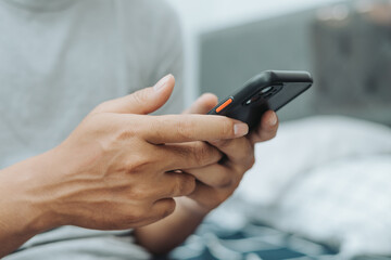 Hands of Asian man holding checking touching scrolling smartphone from bed room