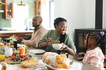 Happy african american mother serving food for daughter at thanksgiving dinner