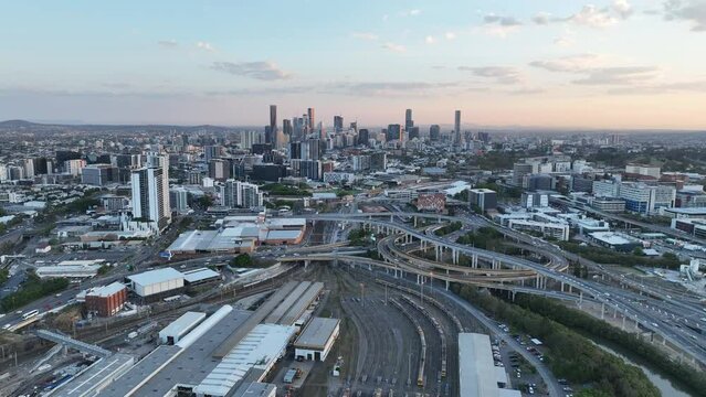 Establishing pull away drone shot of Brisbane City, with Mayne Railway Yard and the ICB inner city bypass. Shot during sunset, city Skyline standing tall against lovely sunset sky.