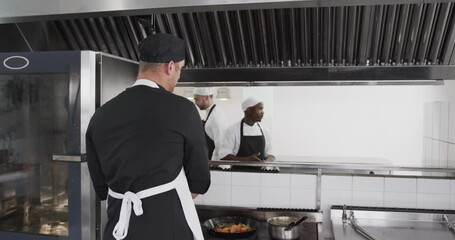 Focused diverse male chef instructing trainee male chefs in kitchen, slow motion