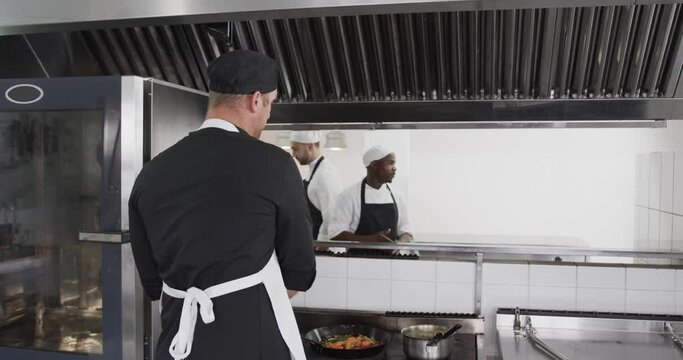 Focused diverse male chef instructing trainee male chefs in kitchen, slow motion