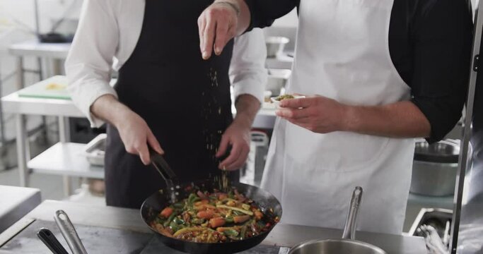 Caucasian male chef instructing trainee male chef in kitchen, slow motion