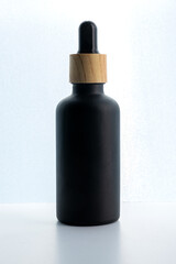 Dark frosted glass cosmetic bottle with a dropper on a black background. Natural cosmetics concept, natural essential oil and skin care products, mockup