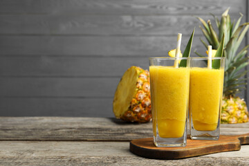 Tasty pineapple smoothie and cut fruit on wooden table, space for text