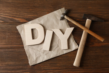 Abbreviation DIY made of letters and hammers on wooden table, flat lay