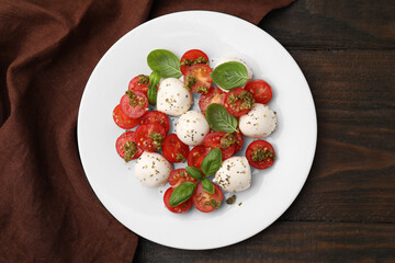 Tasty salad Caprese with tomatoes, mozzarella balls and basil on wooden table, top view