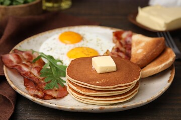 Tasty pancakes served with fried eggs and bacon on wooden table, closeup