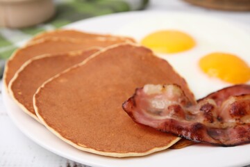 Tasty pancakes with fried eggs and bacon on white wooden table, closeup