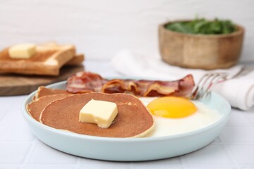 Tasty pancakes served with fried egg and bacon on white tiled table, closeup