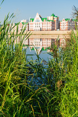 Yoshkar-Ola, Russia. Green grass on the banks of the Malaya Kokshaga river. In the background, houses on the embankment name Amsterdam