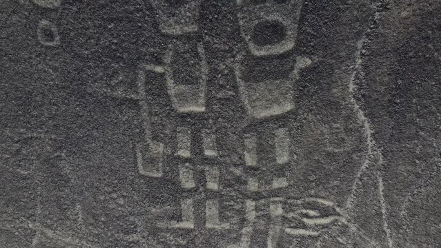 Close up view of Two human figures nearly cartoon like camera rising up to reveal the hill of the Nazca Lines geoglyphs made in the soil of the Nazca Desert Aerial video