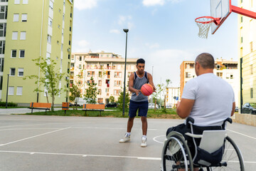 Mature man in the wheelchair coaching basketball to a young black man at the youth center before tryouts