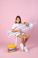 Cheerful schoolgirl with a huge pencil on pink background.
