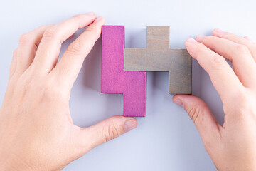 Hand holding wooden puzzle element. Hand sets the last element of the puzzle. The concept of logical thinking. Geometric shapes on a wooden background. Wooden blocks.