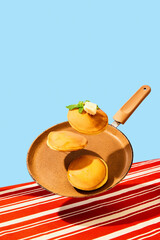 Food pop art photography. Close up. Flying frying pan with hot, sweet, delicious pancakes and butter. Vintage, retro 80s, 70s style, interior. Complementary colors.