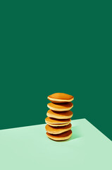 Breakfast time. Food pop art photography. Freshly prepared delicious sweet pancakes over green background. Complementary colors.