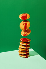 Food pop art photography. Close up. Flying sweet pancakes with delicious jam over green background. Vintage, retro 80s, 70s style, interior. Complementary colors.