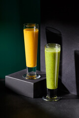 Minimalistic composition of vibrant green and orange smoothies in tall glasses, poised on podiums...