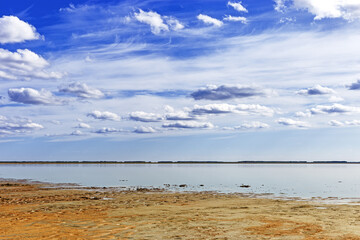 Fototapeta na wymiar Scenic summer landscape blue sky clouds, water surface and sandy shore. Minimal aesthetic nature view. Pastel colors cloudscape. Ulzhay (Uldjay) salt lake with medicinal mud in Omsk region