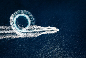 Aerial top view of a motor powerboat forming a circle of waves and bubbles with its engines over the blue sea