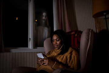 Ghost looking through window at woman using mobile phone in cabin