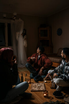 Terrified multiracial friends with ouija board looking at ghost in cabin