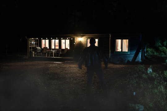 Silhouette demon in front of illuminated cabin at night