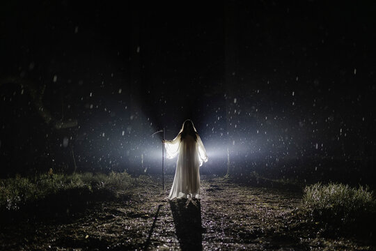 Ghost with scythe standing in forest at night during rainy season