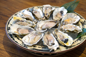 A bounty of fresh oysters resting on crushed ice within a rustic bowl. The bowl is positioned at the center of wooden table.
